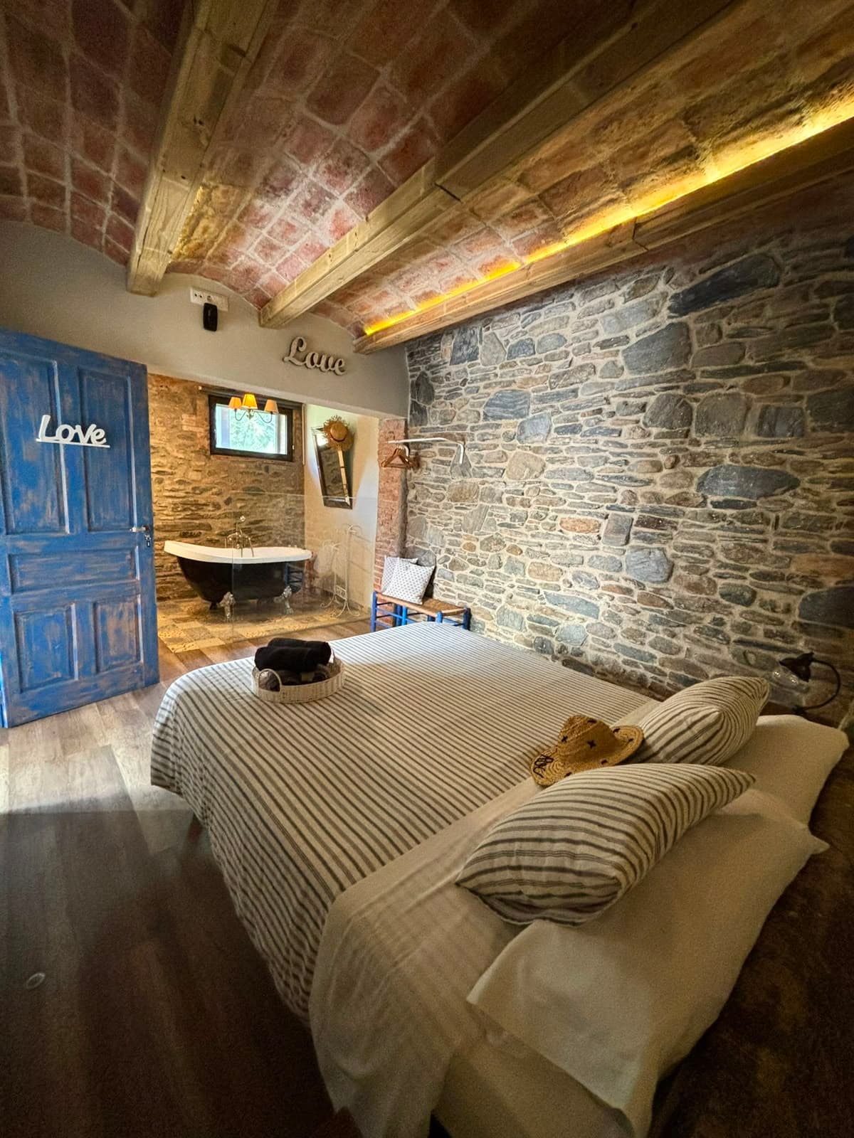 Vista de l'Habitació Love amb el llit en primer terme i la banyera exempta al fons, al costat de la porta blava