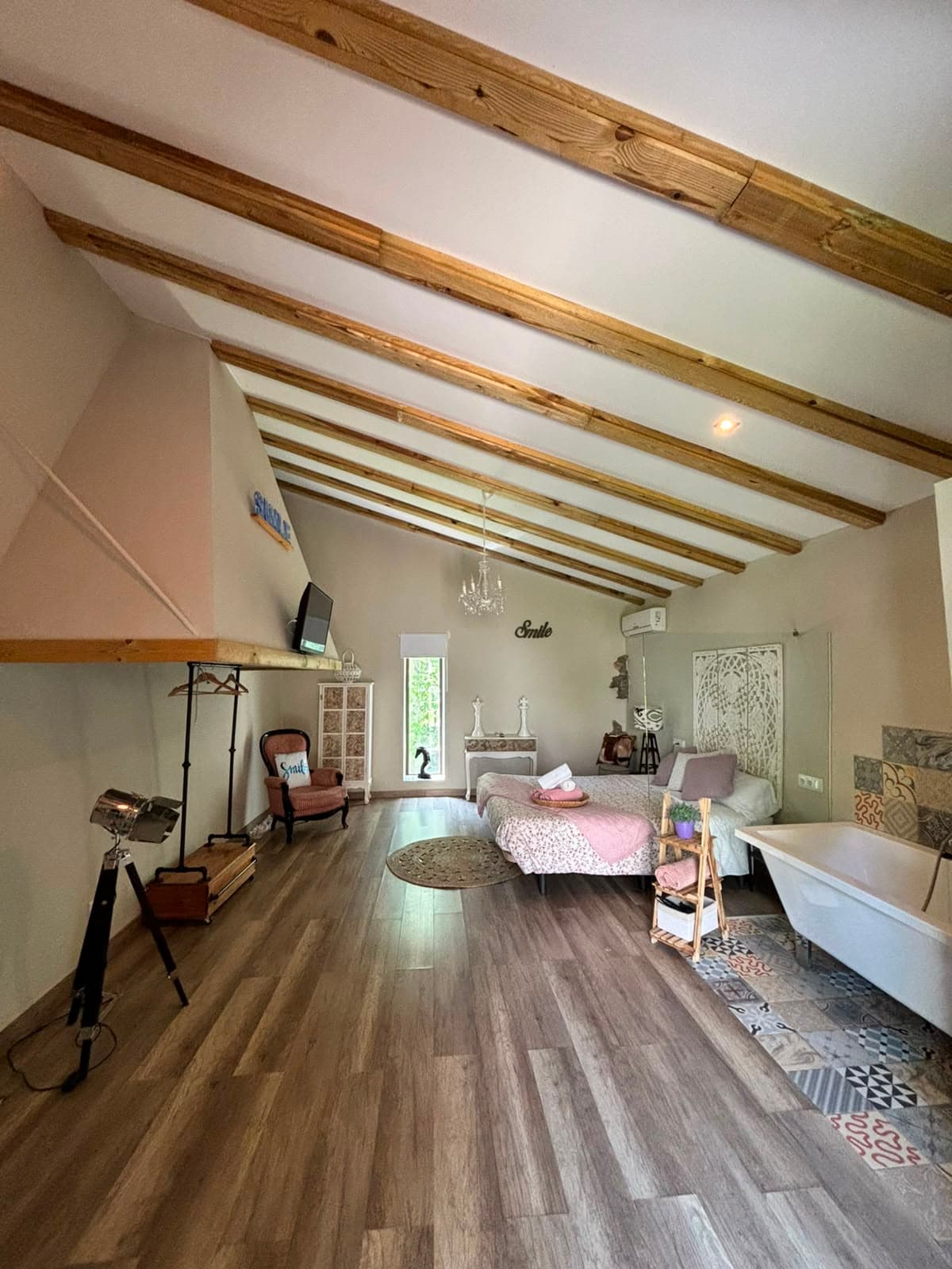 Vista general de l'Habitació Smile, amb el llit, el sofà i la banyera exempta al fons sota el sostre de bigues de fusta